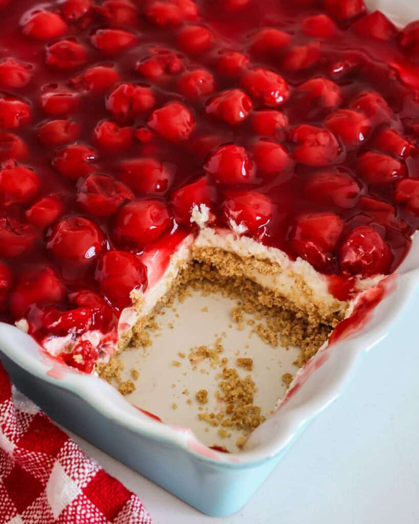 A 9x9 inch casserole dish full of cherry delight with one slice missing. 