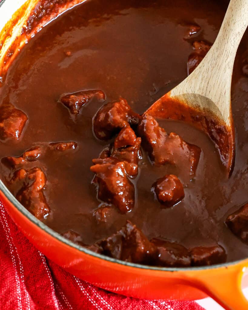 A large orange Dutch oven full of Chile Colorado. 