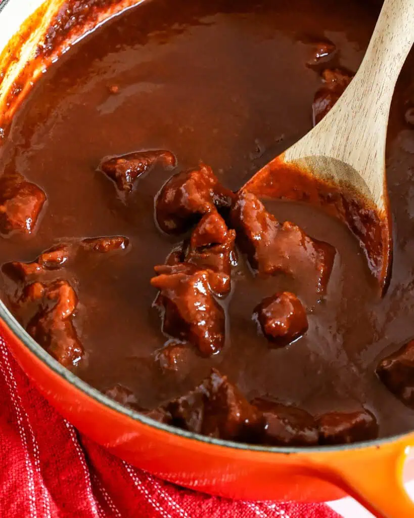 A large orange Dutch oven full of Chile Colorado. 