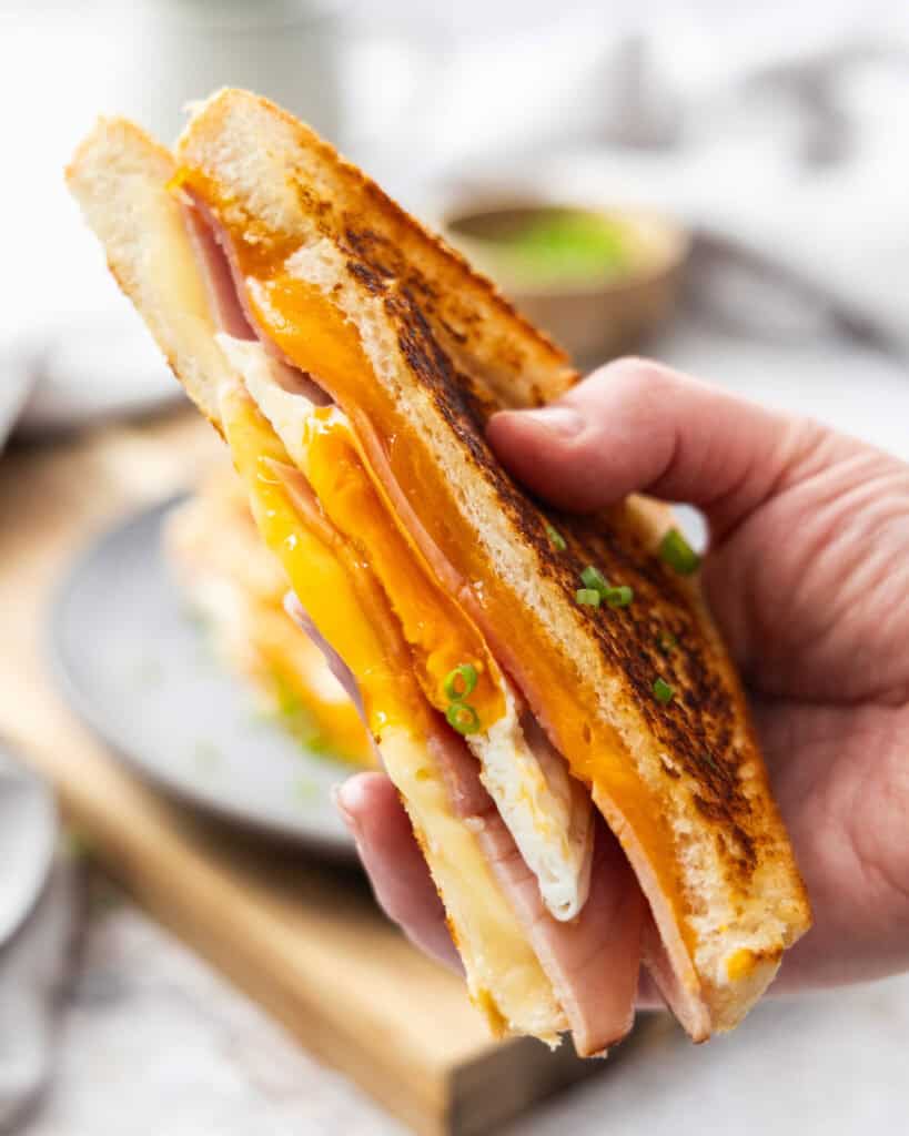 A cut fried egg sandwich held up by a hand.