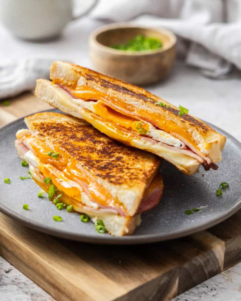 A breakfast sandwich stacked on a gray plate on a cutting board.