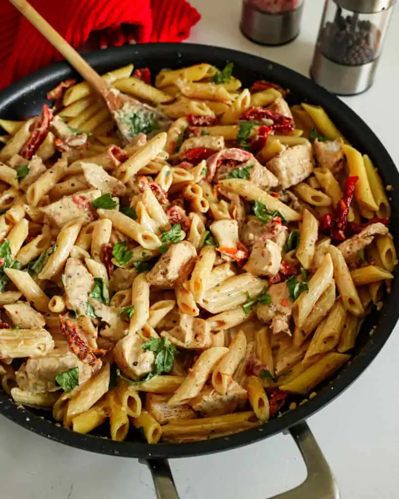 A skillet full of Marry Me Chicken pasta with sundried tomatos and fresh basil in a creamy Parmesan sauce. 
