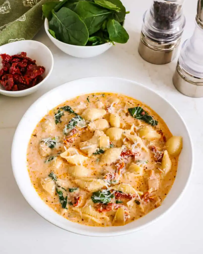 A single serving bowl full of Marry Me Chicken Soup with bowls full of spinach, sundried tomatoes, and salt and pepper shaker in the background. 