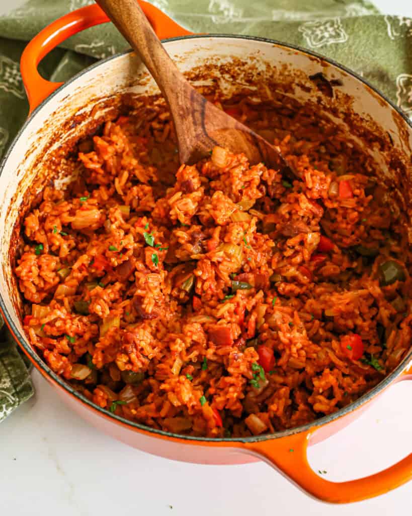 A Dutch oven full of fresh baked Charleston red rice with a wooden spoon in it. 