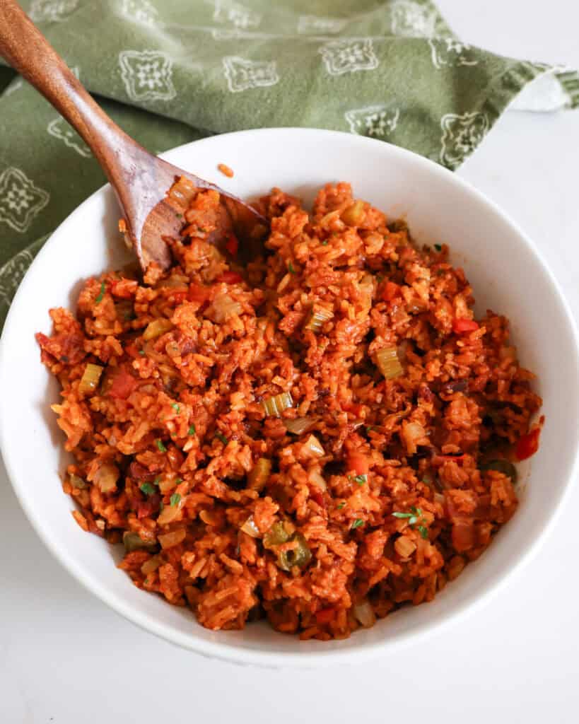 A round white serving dish full of Charleston red rice with a wooden serving spoon.
