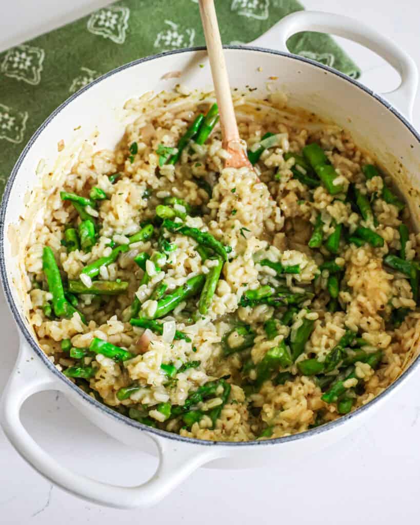 A braiser full of asparagus risotto with a wooden spoon in it.