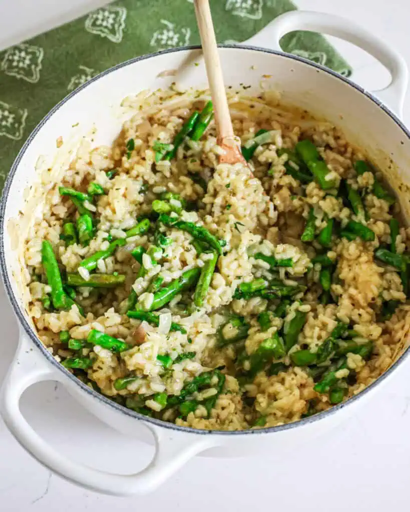 A braiser full of asparagus risotto with a wooden spoon in it. 