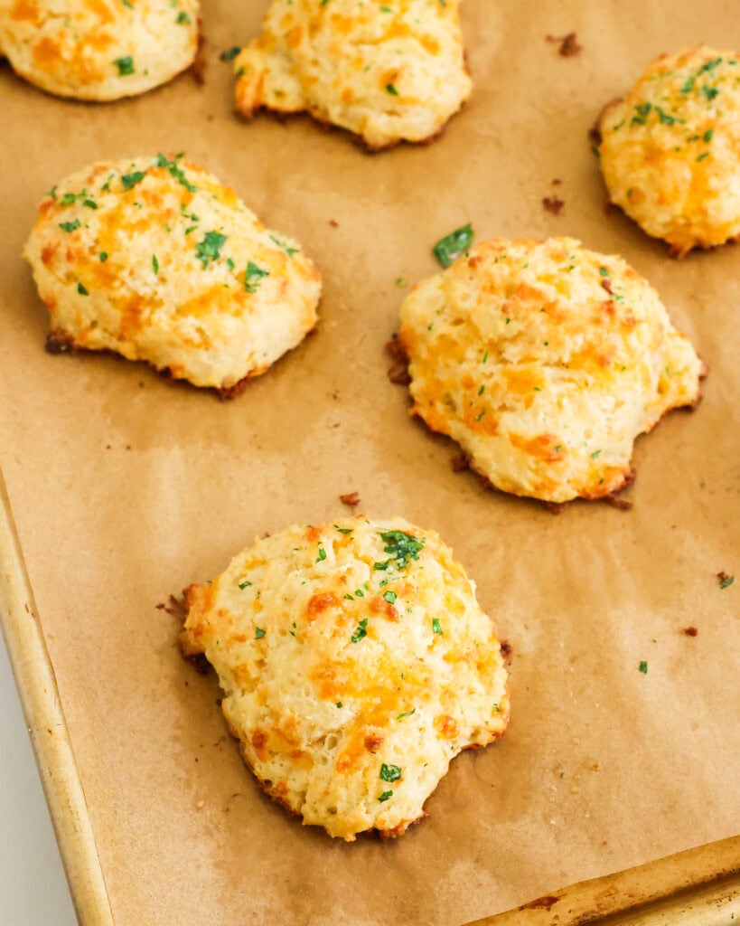 Fresh baked cheddar bay biscuits on a parchment paper lined baking sheet.