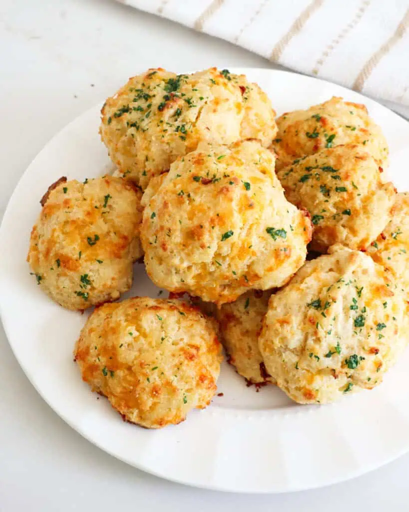 Freshly baked homemade cheddar bay biscuits on a round white serving plate. 