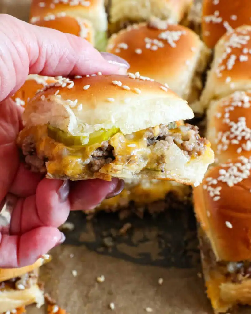 A close up view of someone holding a cheeseburger slider with pickles. 