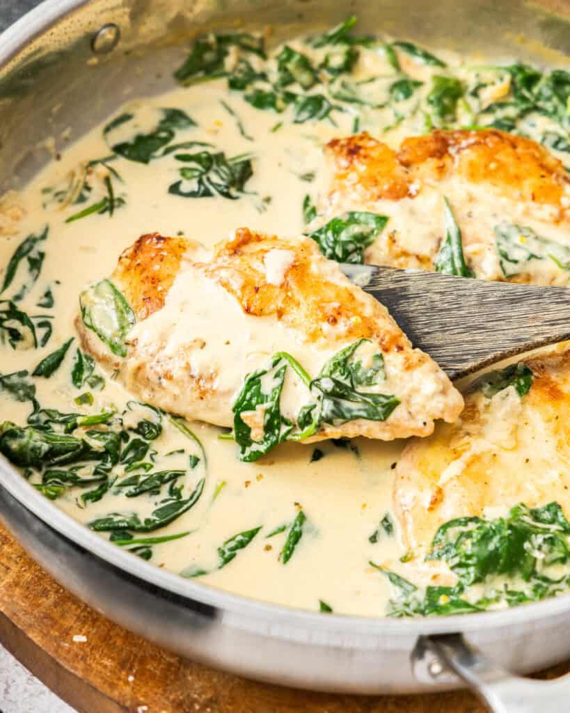 A skillet full chicken floretine and a close up view of a piece of chicken florentine on a wooden spatula. 