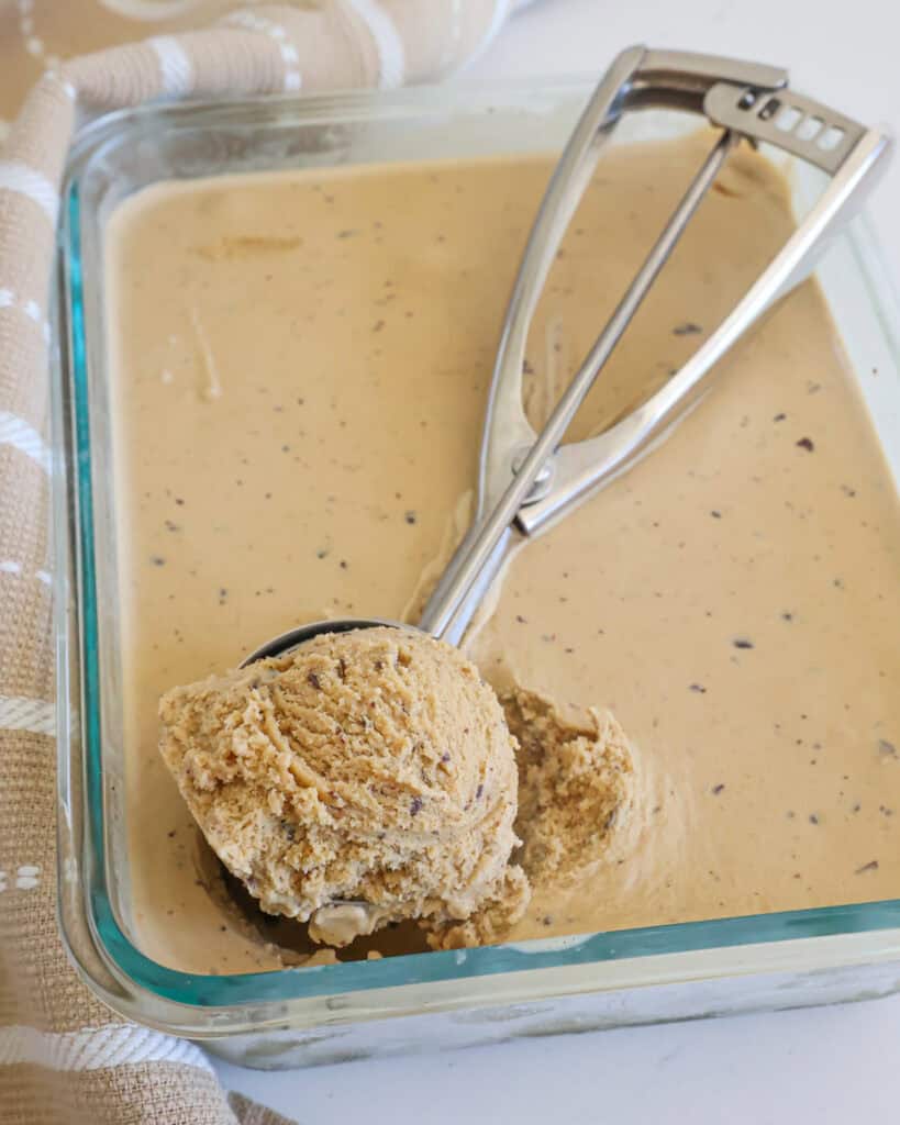 A Pyrex dish full of coffee ice cream with an ice cream scoop in it with a scoop of coffee ice cream in it.