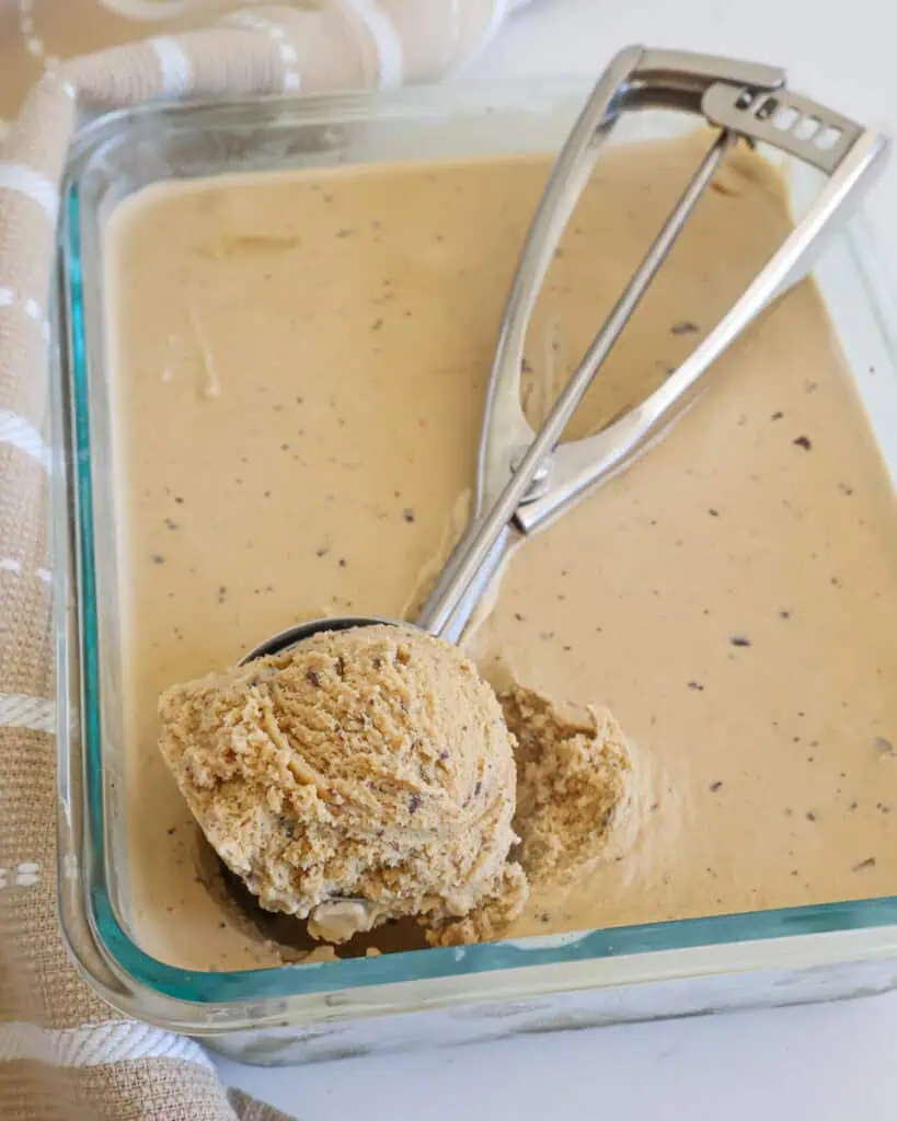 A Pyrex dish full of coffee ice cream with an ice cream scoop in it with a scoop of coffee ice cream in it. 
