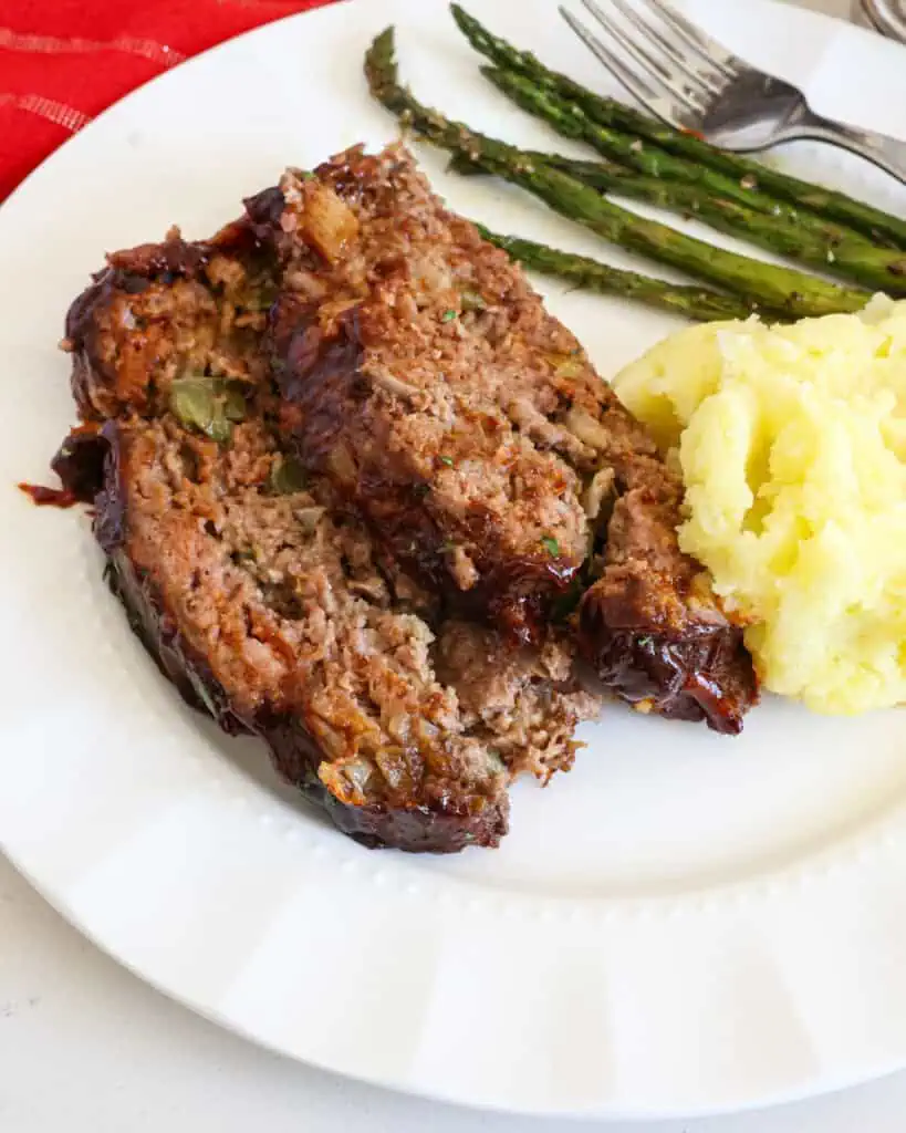 Two slices of Cracker Barrel meatloaf on a plate with mashed potatoes and asparagus. 
