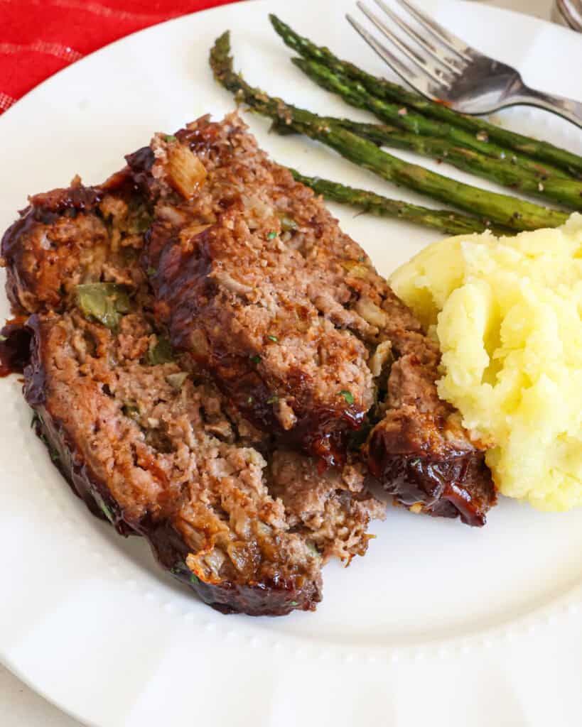 A close up view of Cracker Barrel Meatloaf on a white plate with mashed potatoes and asparagus.