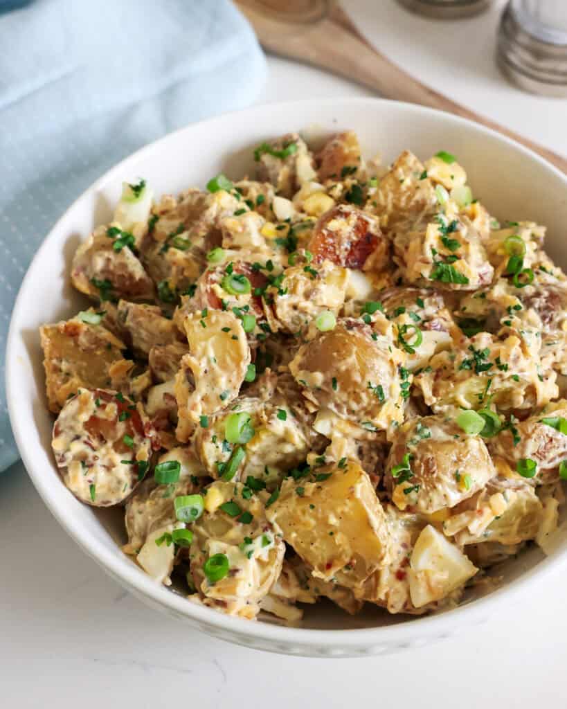 A close up view of loaded baked potato salad in a white serving bowl. 