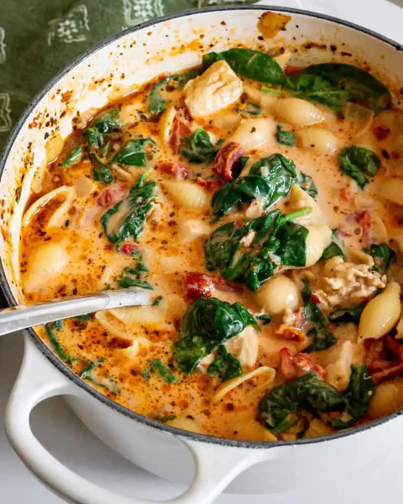A Dutch oven full of Marry Me Chicken Soup with sundried tomatoes, spinach, pasta, onions, and garlic. 
