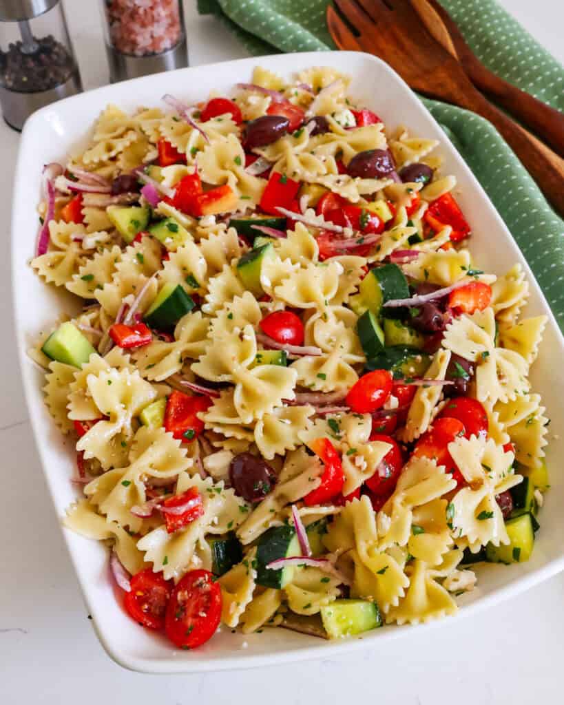 Greek pasta salad in a large serving bowl with wooden tongs and salt and pepper shaker in the background.