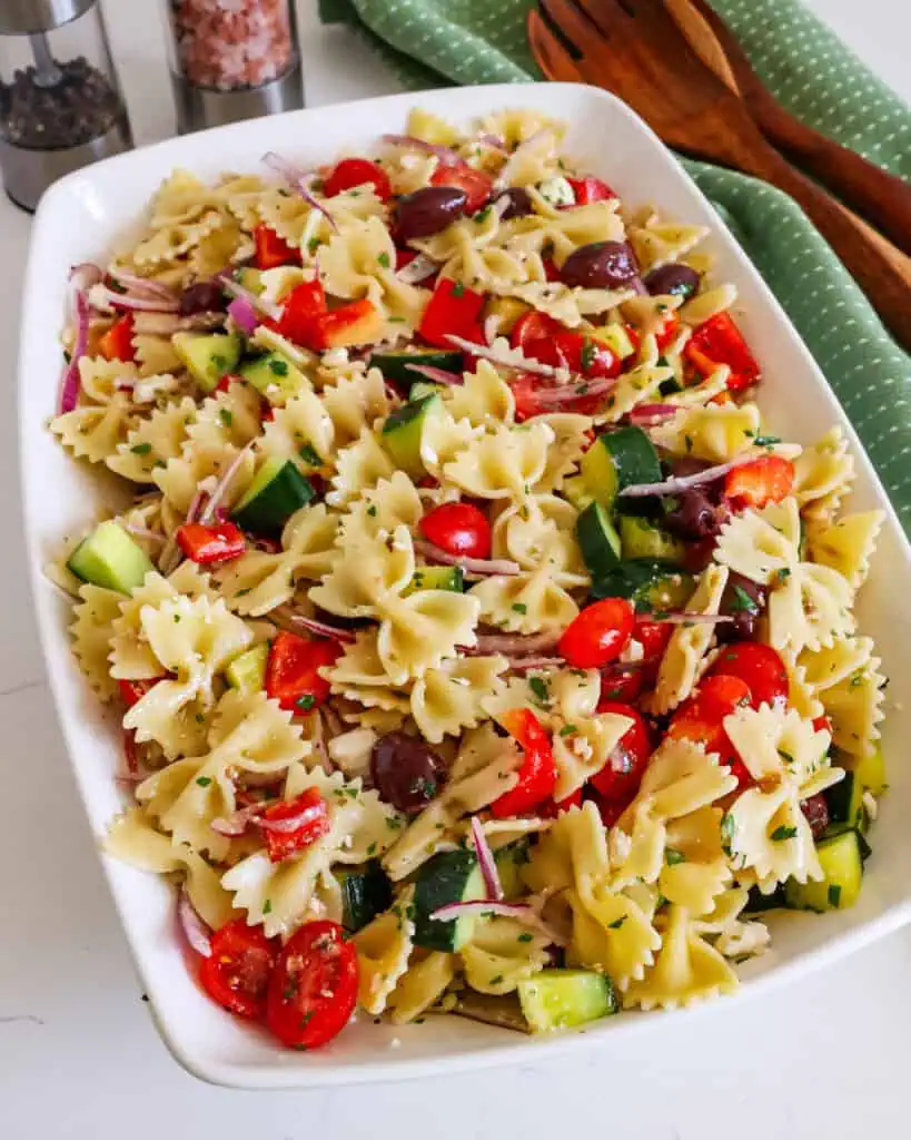Greek pasta salad in a large serving bowl with wooden tongs and salt and pepper shaker in the background. 