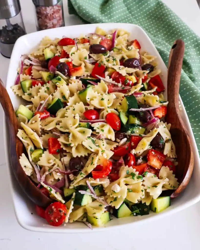 Greek pasta salad in a serving bolw with wooden tongs. 