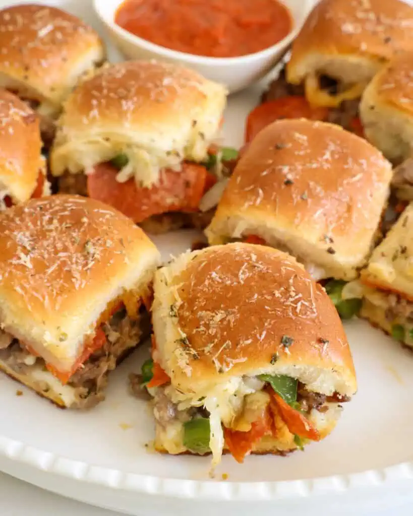 A close up veiw of platter full of pizza sliders with Italian sausage, pepperoni, onions, and green bell peppers. 
