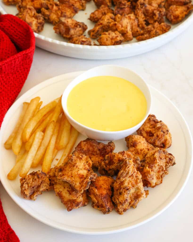 A single serving plate full of popcorn chicken, golden French fries, and honey mustard. 