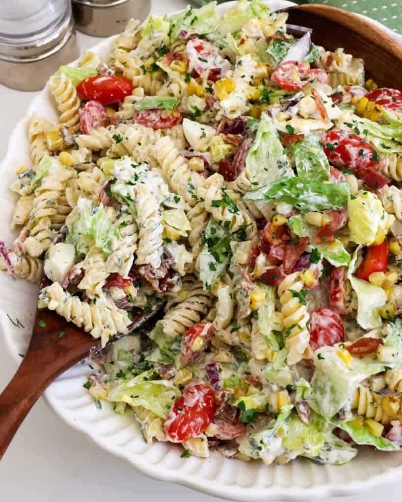 A close up view of BLT pasta salad on a wooden spoon in a large bowl of the salad. 
