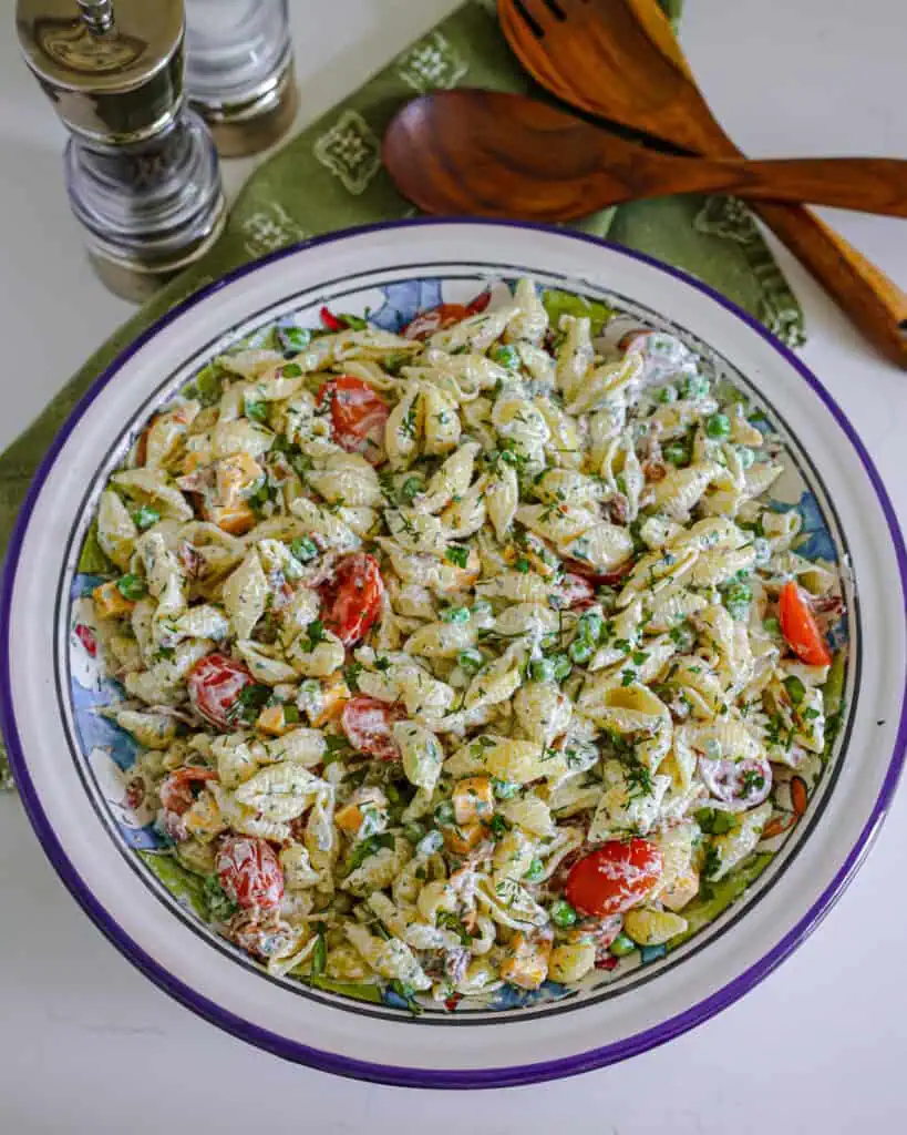 An overhead view of a bog bowl full of bacon ranch pasta salad, wooden serving tongs, and a salt and pepper shaker. 