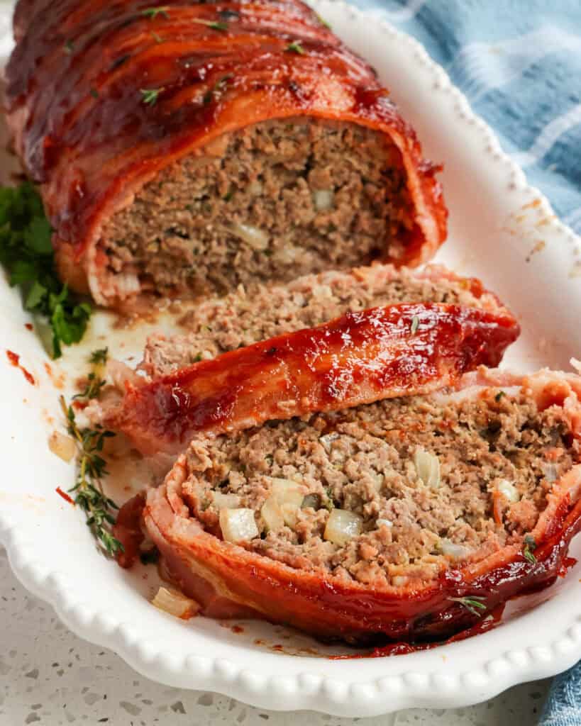 Sliced bacon wrapped meatloaf on a white serving platter.