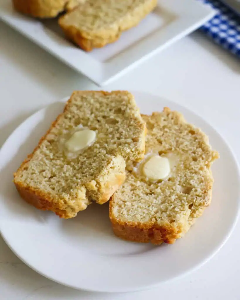 Two slices of beer bread with butter pats on a single serving white plate.