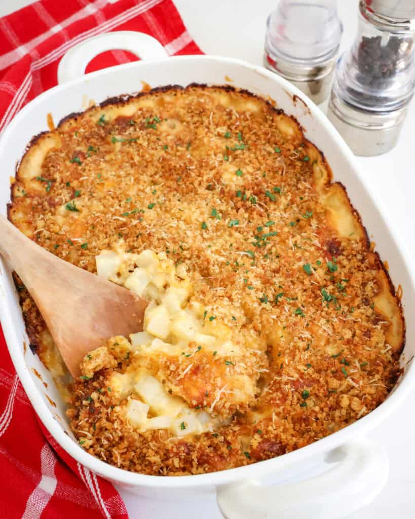 An overhead view of a casserole dish and a wooden spoon full of cheesy potato casserole. 