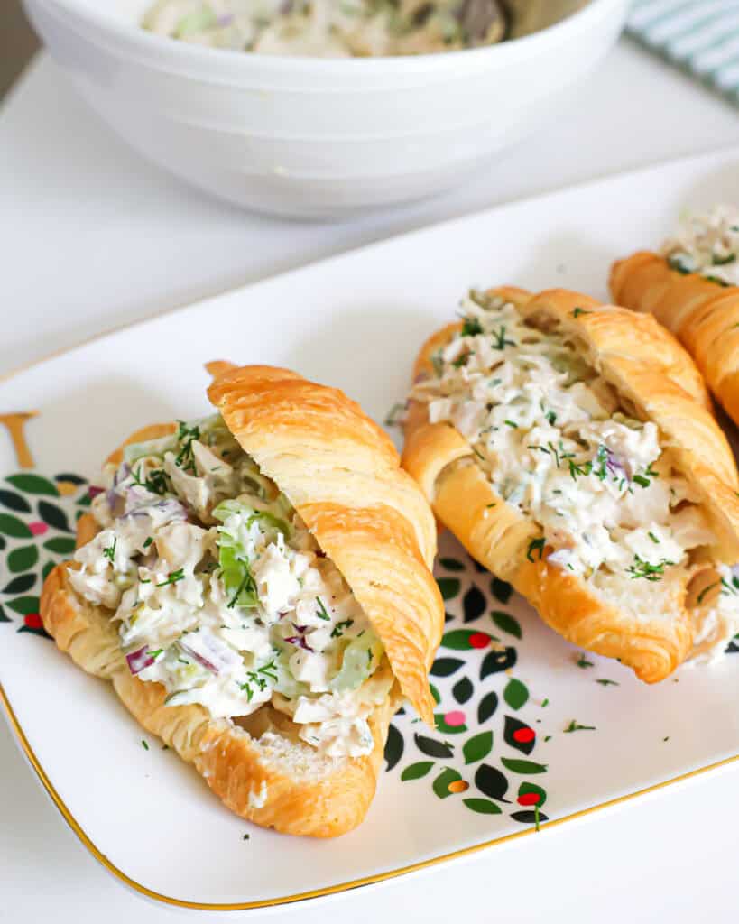 An overhead view of croissants filled with dill pickle chicken salad with a bowl of dill pickle chicken salad in the background. 