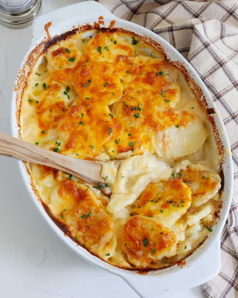An overhead view of a casserole dish and a woode spoon full of au gratin potatoes. 