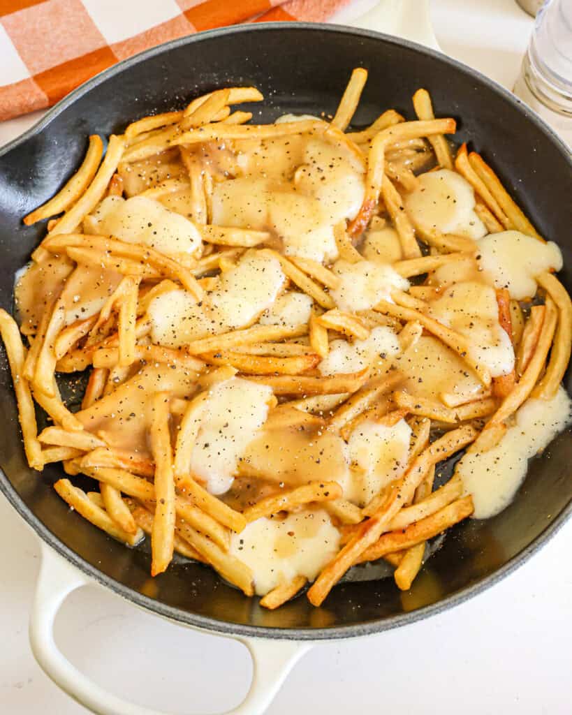 Poutine in a large skillet with a salt and pepper shaker in the background. 