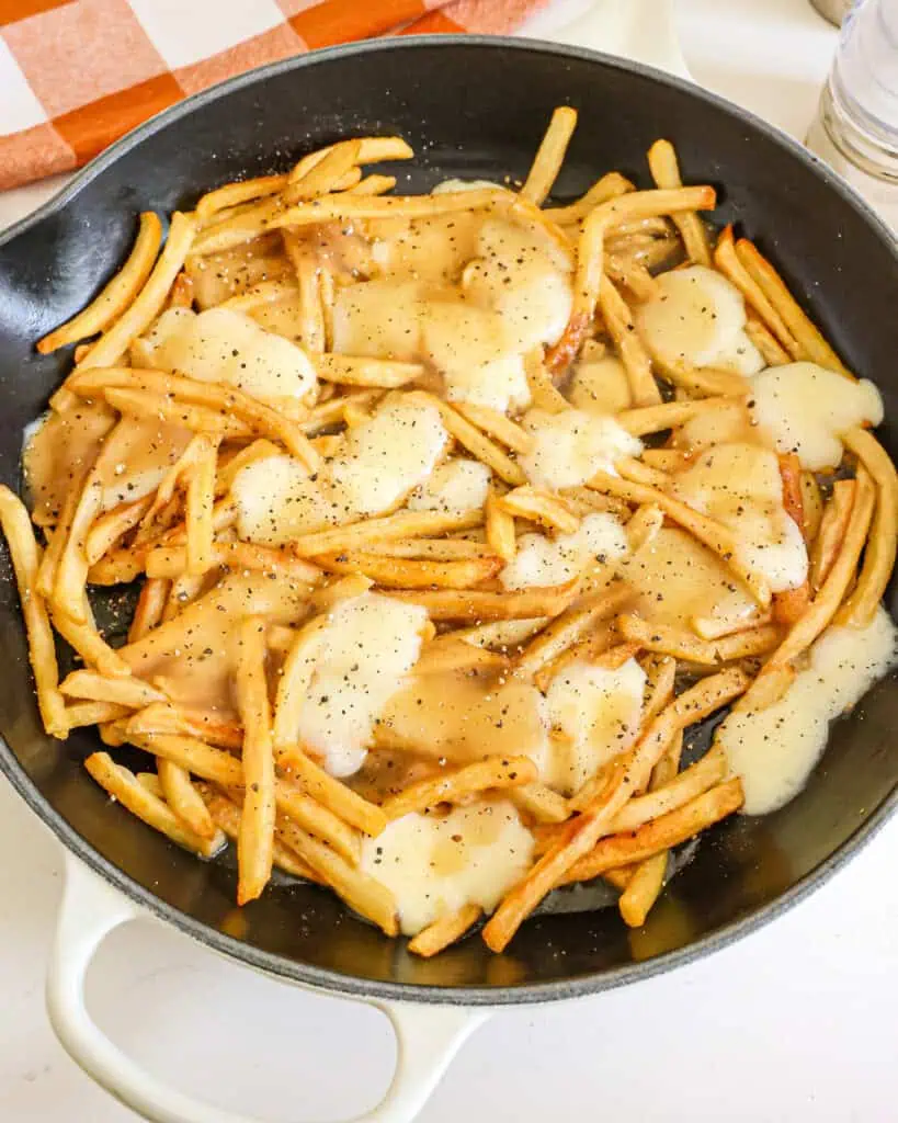 Poutine in a large skillet with a salt and pepper shaker in the background.