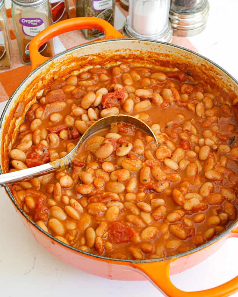 A Dutch oven and a ladle full of ranch style beans. 