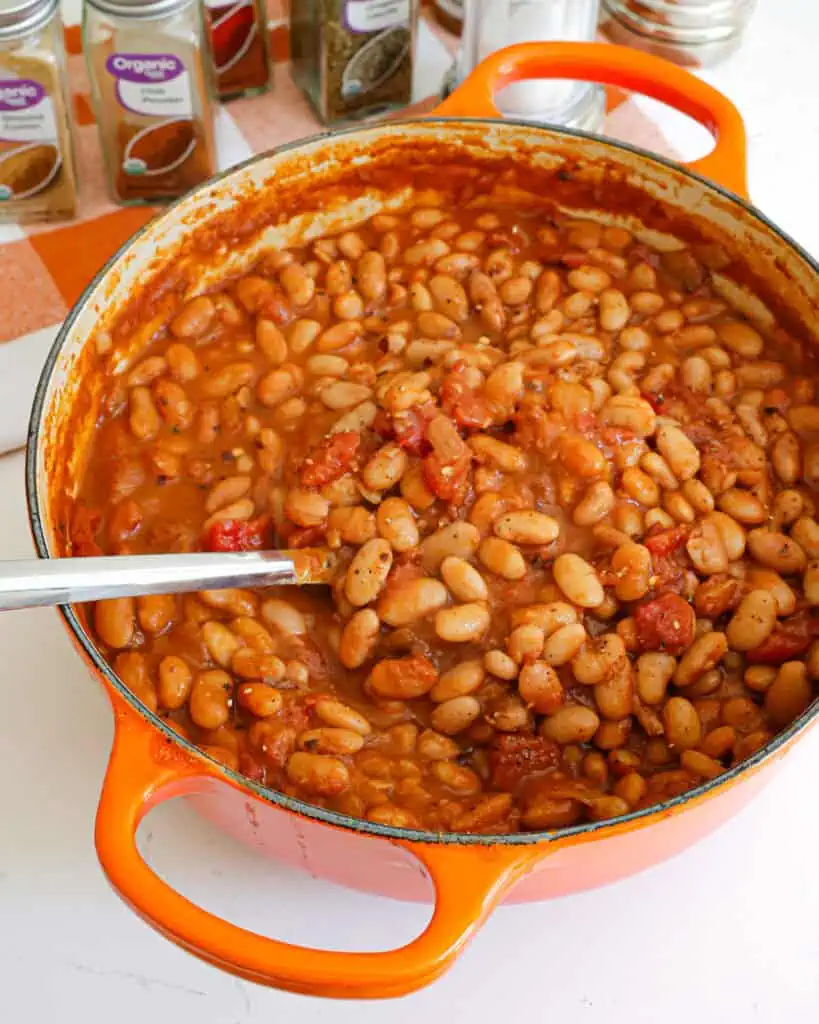 A Dutch oven full of ranch style beans with various spice jars and salt and pepper in the bacckground. 