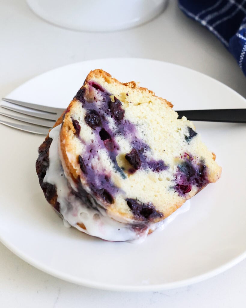 A slice of blueberry bundt cake on a white serving plate with a fork.
