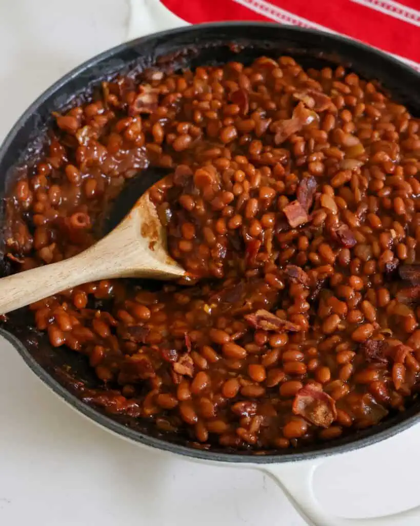 A large cast iron skillet full of baked beans with bacon, onions, and garlic. 