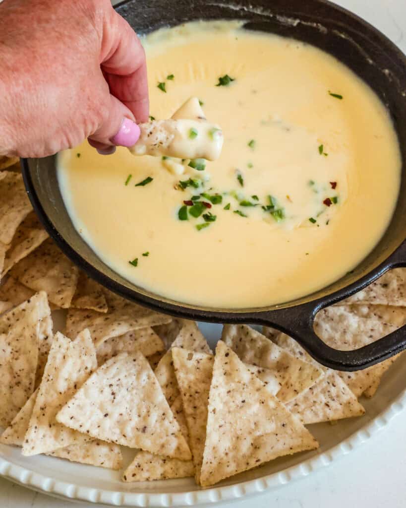 A small ast iron skillet full of cheese dip on a white platter with chips. 