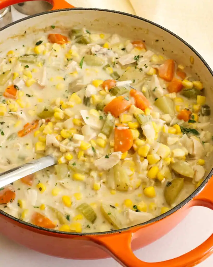 A close up view of chicken corn chowder with onion, celery, carrots, potatoes, corn, and tender chicken in a creamy broth seasoned with fresh thyme and parsley.