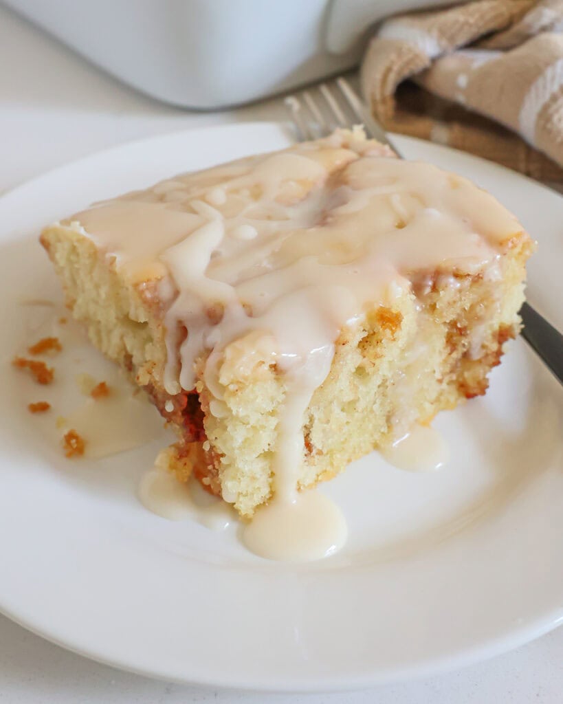 A close up view of a piece of cinnamon roll cake on a plate with a fork. 