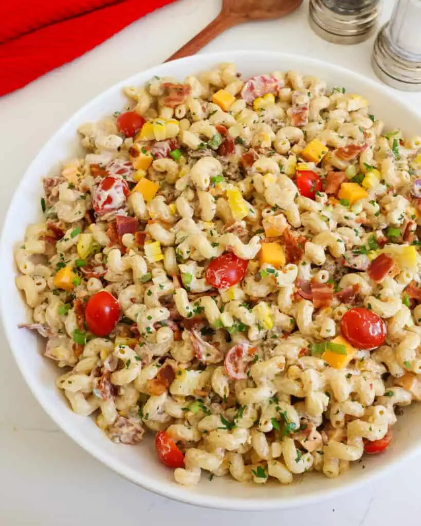 An overhead view of a large serving bowl full of cowboy pasta salad with a large wooden spoon and salt & pepper shaker in the background. 