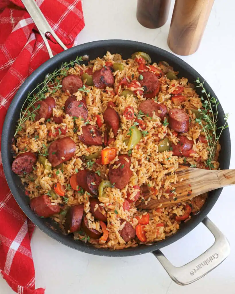 An overhead view of browned smoked sausage with sautéed onions, bell peppers, and garlic alongside fire-roasted tomatoes and rice seasoned with warm Creole herbs and spices. 