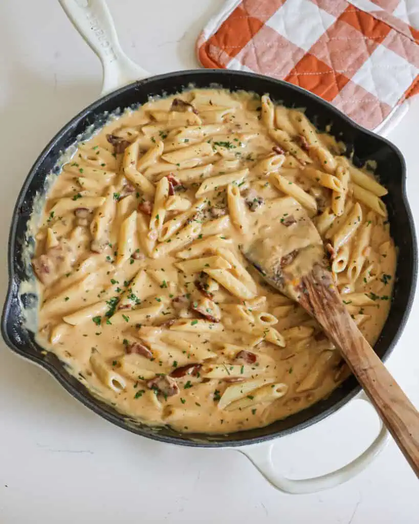 An overhead view of chicken bacon ranch pasta in a skillet with a wooden spoon.