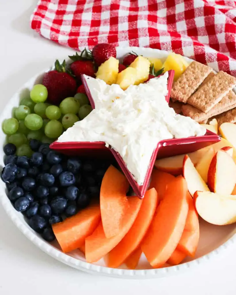 An overhead view of cream cheese dip in a red star bowl with assorted fruit around it. 
