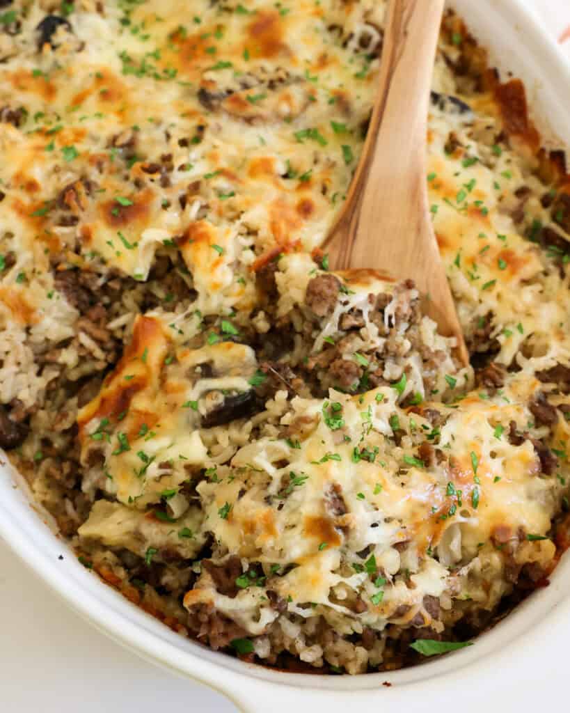 A close up view of a wooden spoon full of hamburger and rice in a casserole dish. 