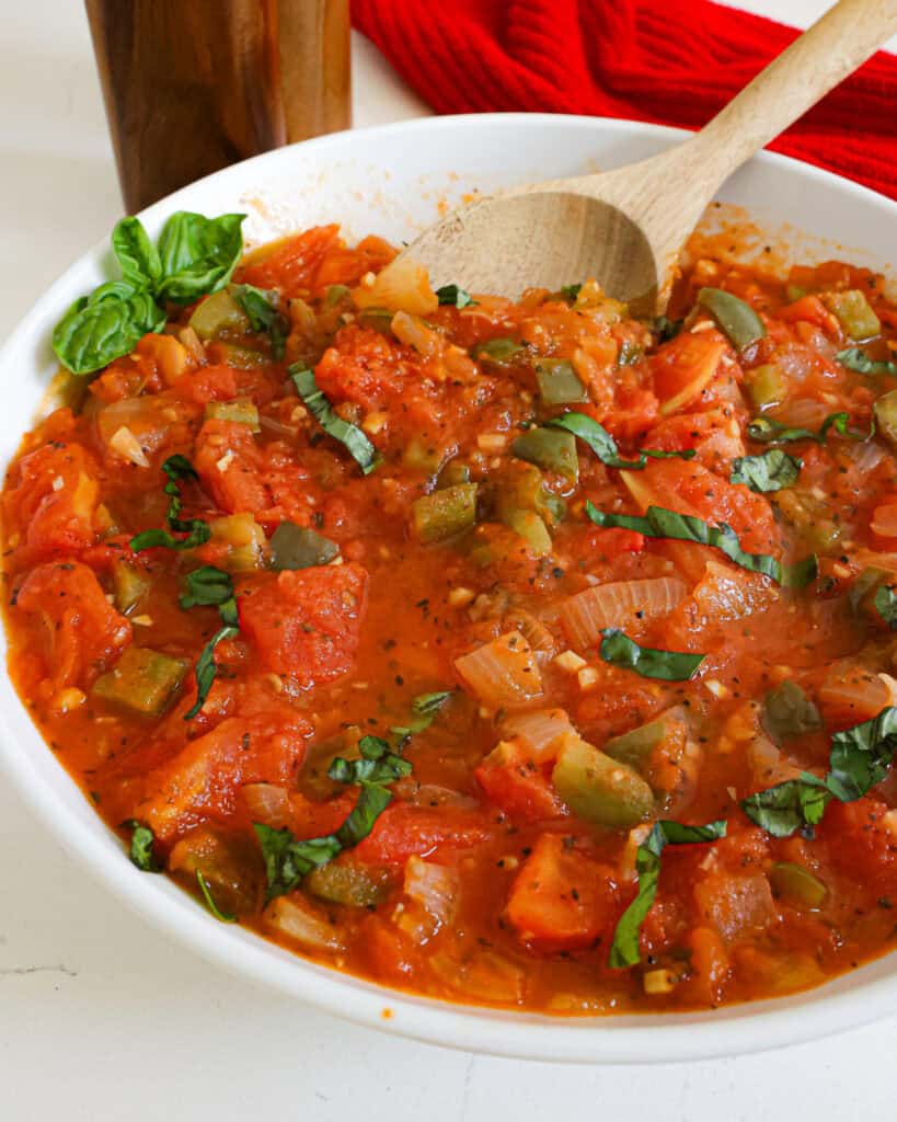 A close up view of stewed tomatoes in a serving bowl with a wooden spoon. 