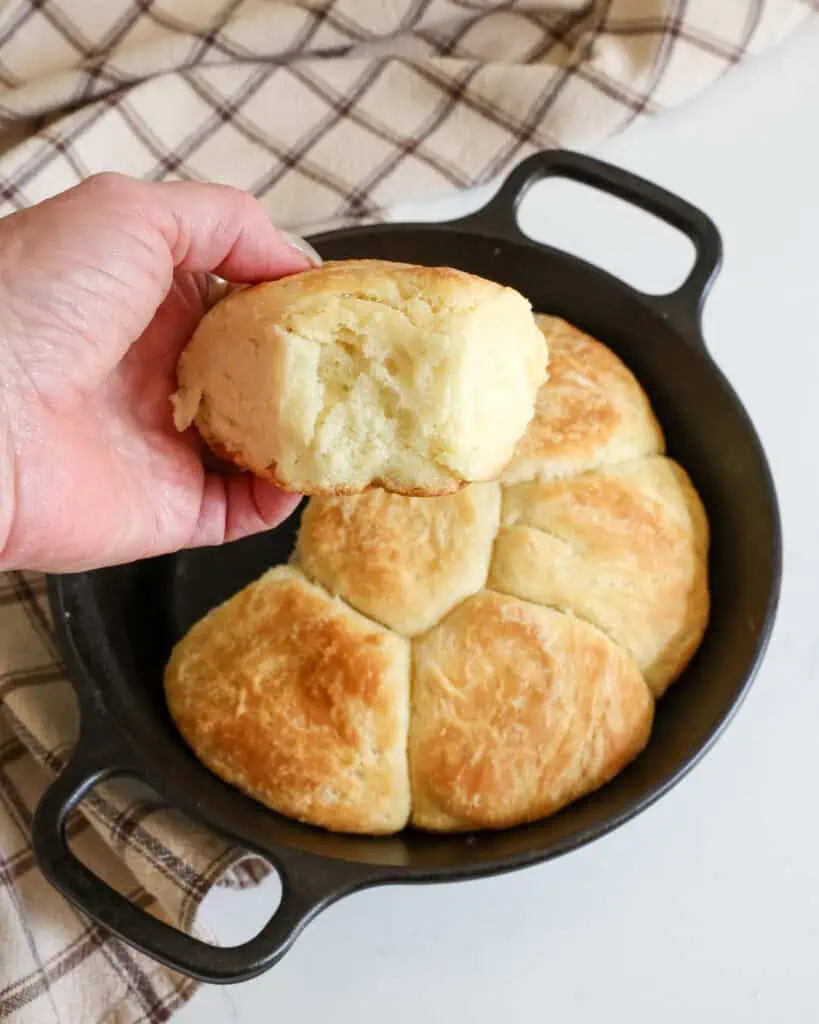 A close up view of any angel biscuit over a small cast-iron skillet full of angel biscuits.