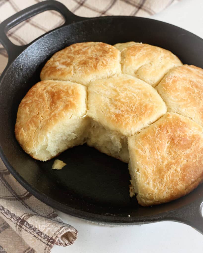 An 8 inch cast iron skillet with 6 angel biscuits in it. 